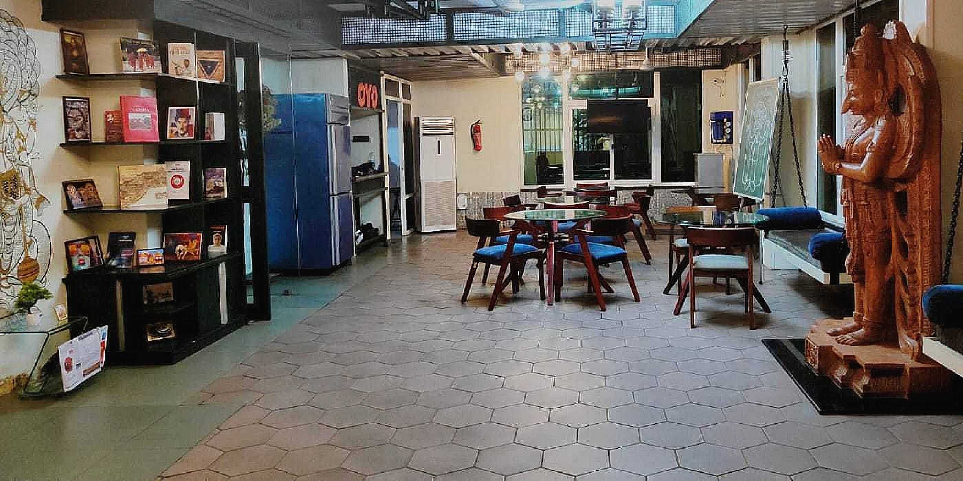 A room with a hexagonal tiled floor, a round table with chairs, a statue, and a bookshelf with various items.