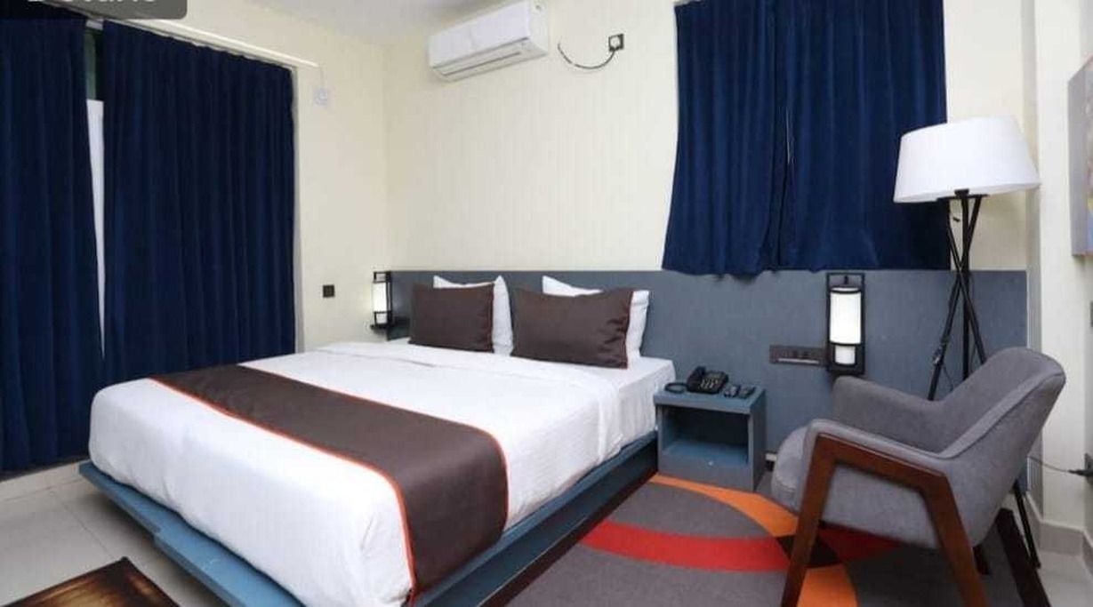 Habitación de hotel con cama, mesita de noche, lámpara, silla y cortinas.