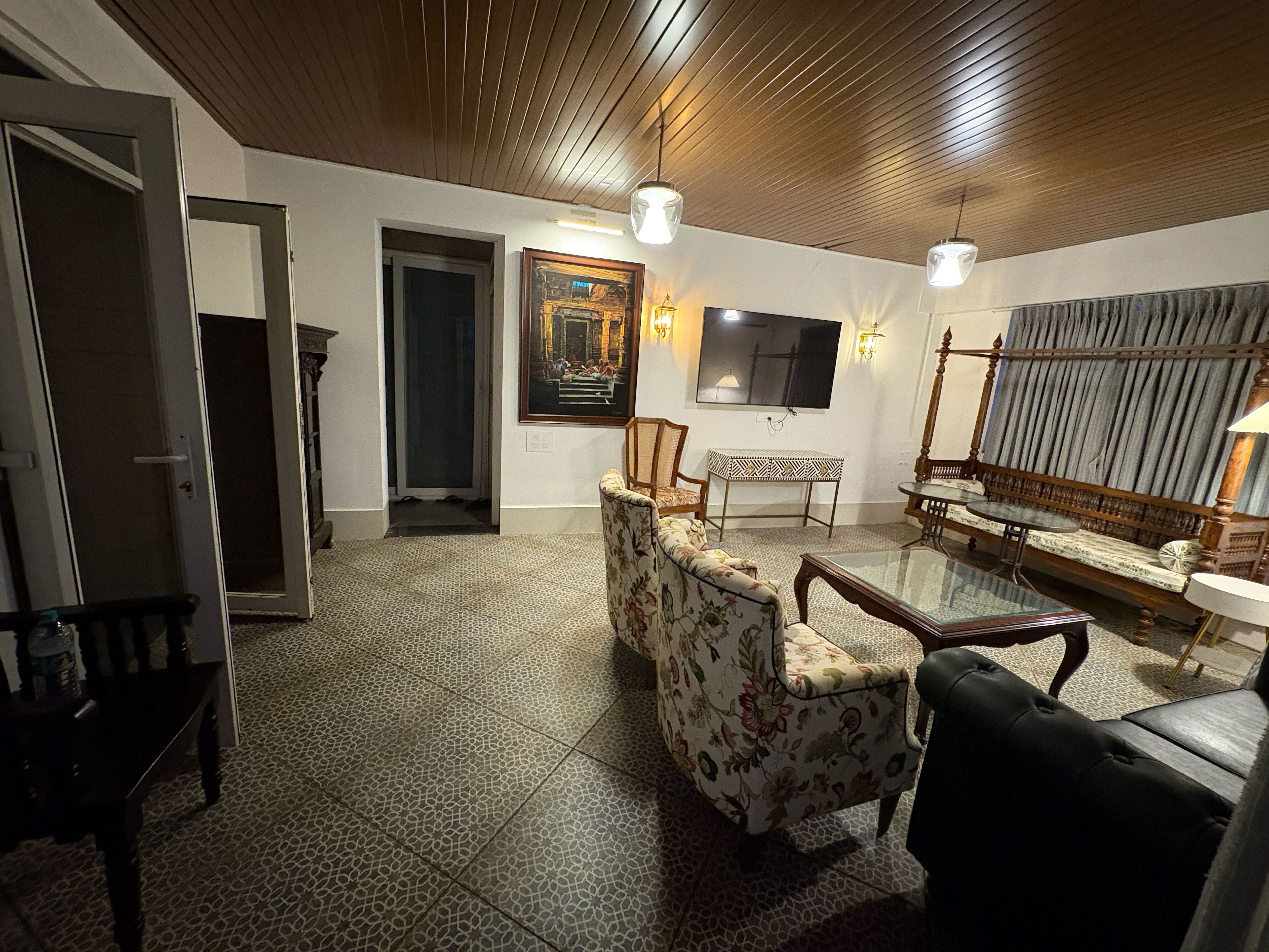 A spacious living area with a high ceiling, a television mounted on the wall, and a patterned floor.