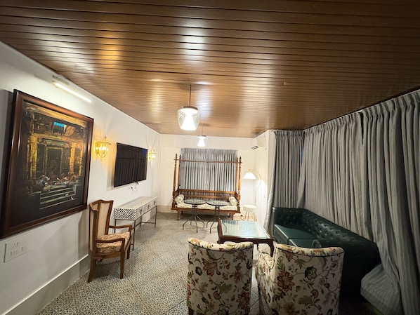 A room with a wooden ceiling, a television mounted on the wall, a sofa, a patterned floor, and a framed painting. - Super Collection O Vastukar Retreat (Bhubaneswar)