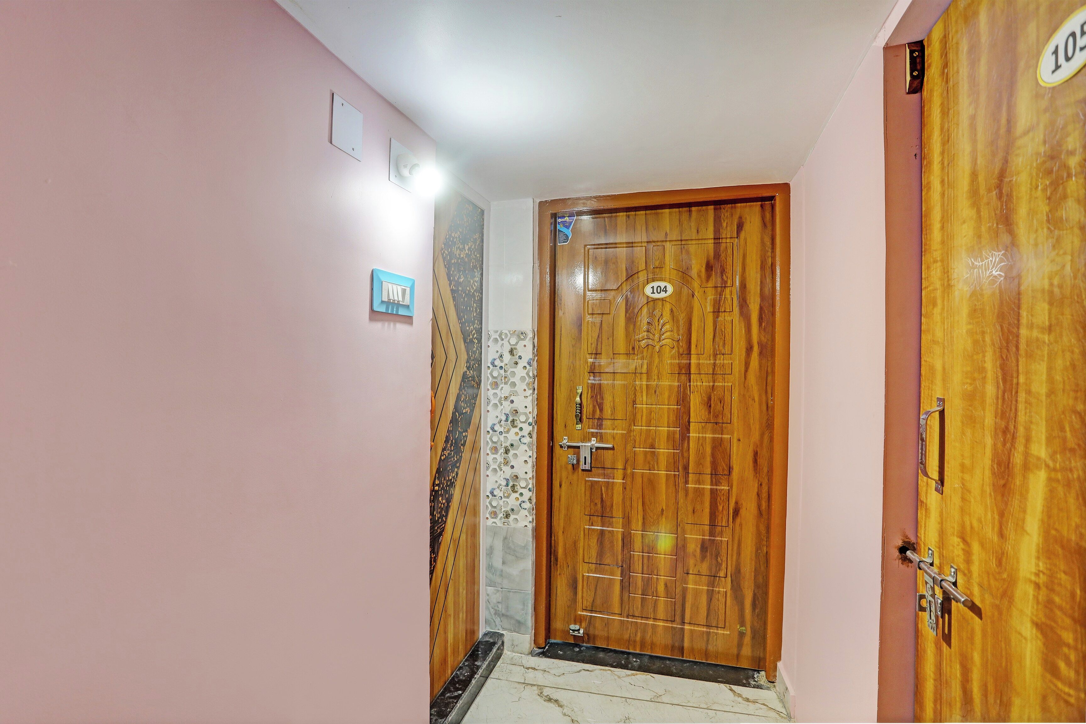 Un pasillo con una puerta de madera marcada con el número '104' e interruptor de luz en la pared.