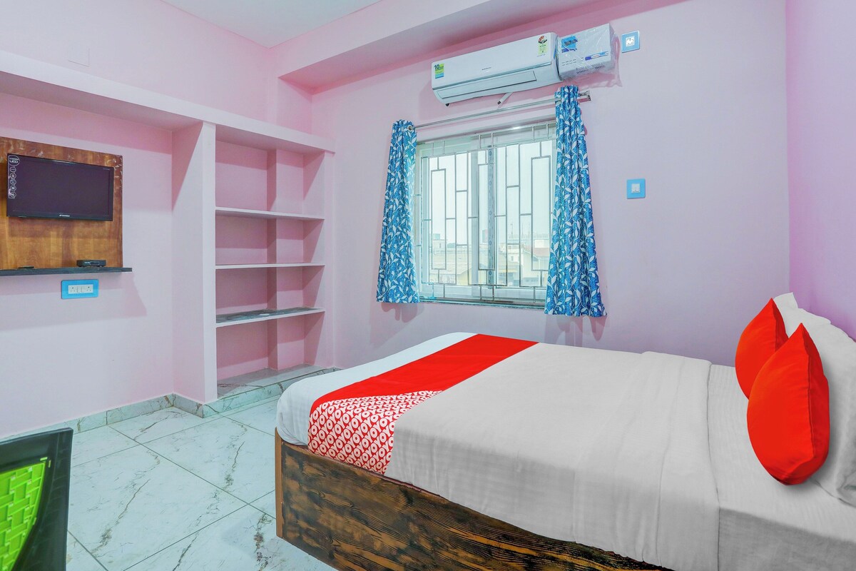 Un dormitorio con cama, televisor montado en la pared, ventana con cortinas y equipo de aire acondicionado.