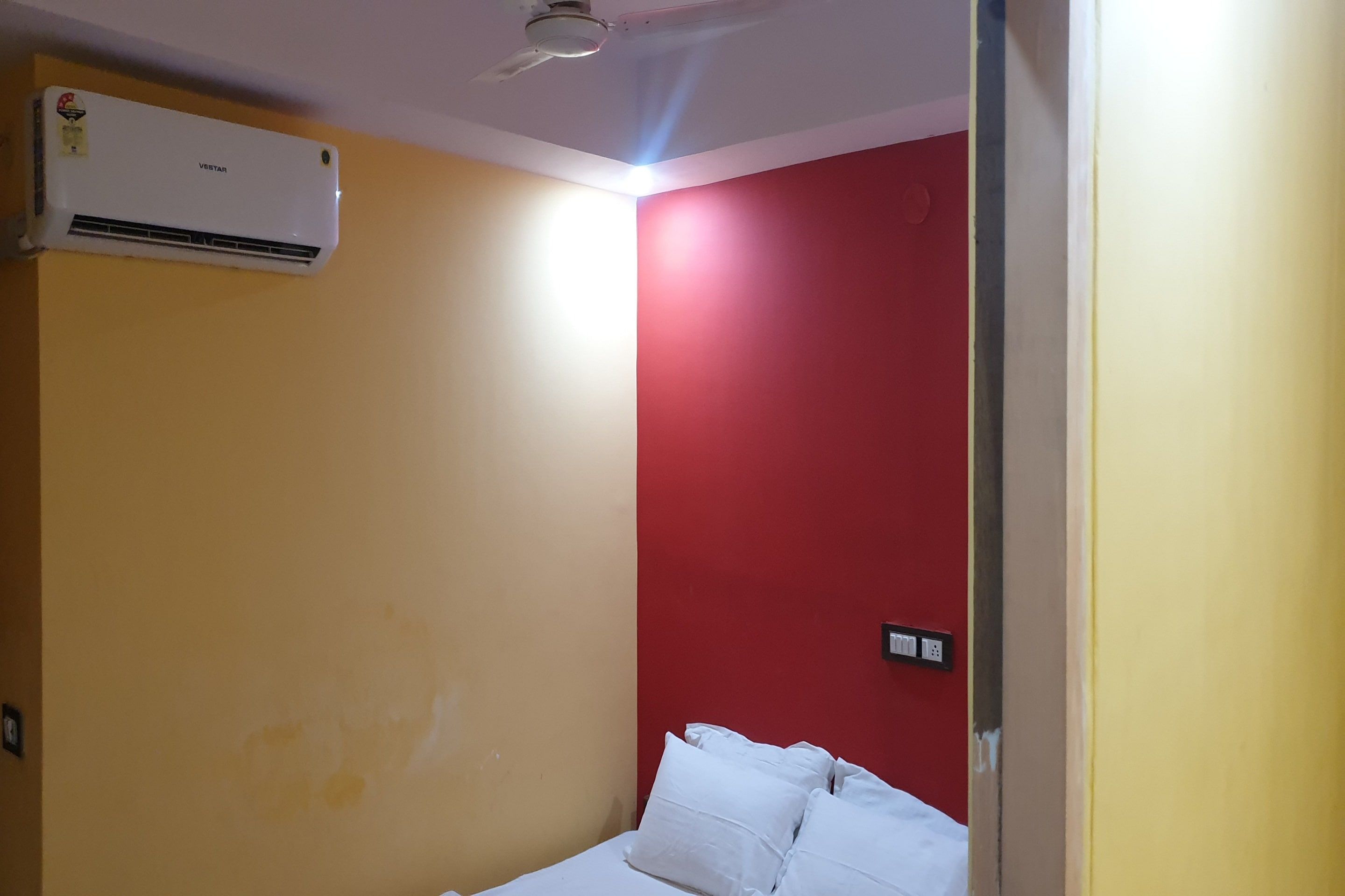 A room with a bed, a wall-mounted air conditioner, and a red accent wall.