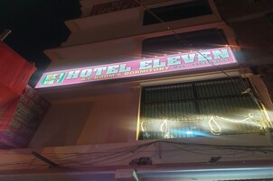 Un edificio con un letrero de neón que dice 'Hotel Eleven', indicando que ofrece habitaciones con aire acondicionado y alojamiento en dormitorios.