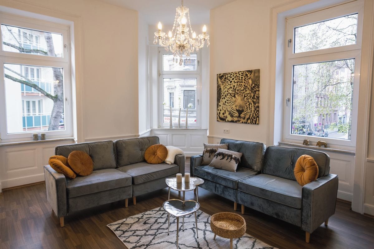 Ein Wohnzimmer mit einem grauen Ecksofa, einer Kristallleuchtre und einem Kunstwerk mit Leopardenmuster.
