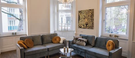 Ein Wohnzimmer mit einem grauen Ecksofa, einer Kristallleuchtre und einem Kunstwerk mit Leopardenmuster.