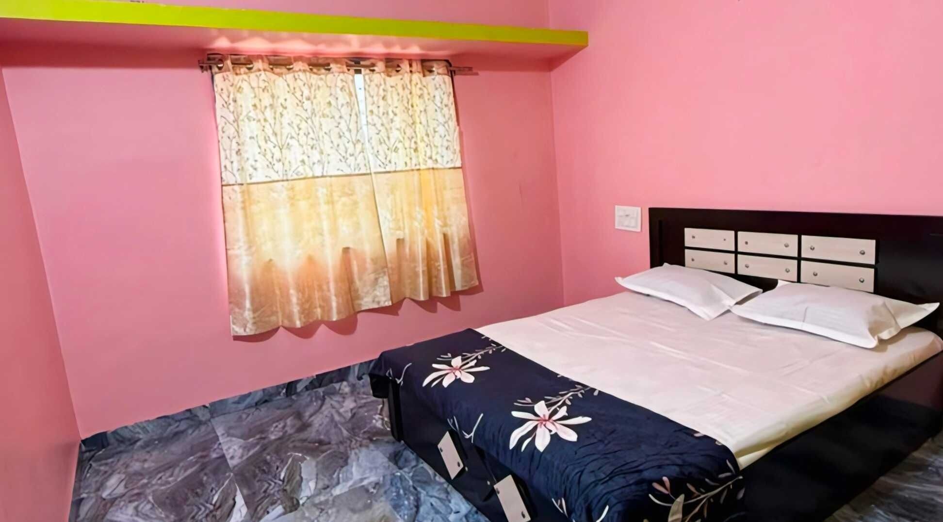A single bed with a headboard, a window with a floral curtain, and a pink wall.