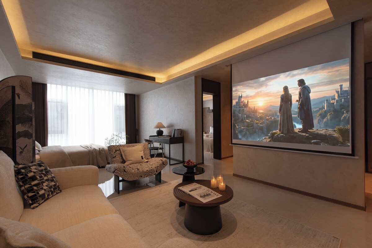 Een moderne hotelkamer met een grote flatscreen-tv, een bank, een gestreept fauteuil, een salontafel en een decoratief wandobject.