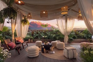 A serene outdoor seating area with a view of mountains, featuring wicker furniture, draped curtains, and hanging lights. - Carefree Garden Hotel (Lijiang)