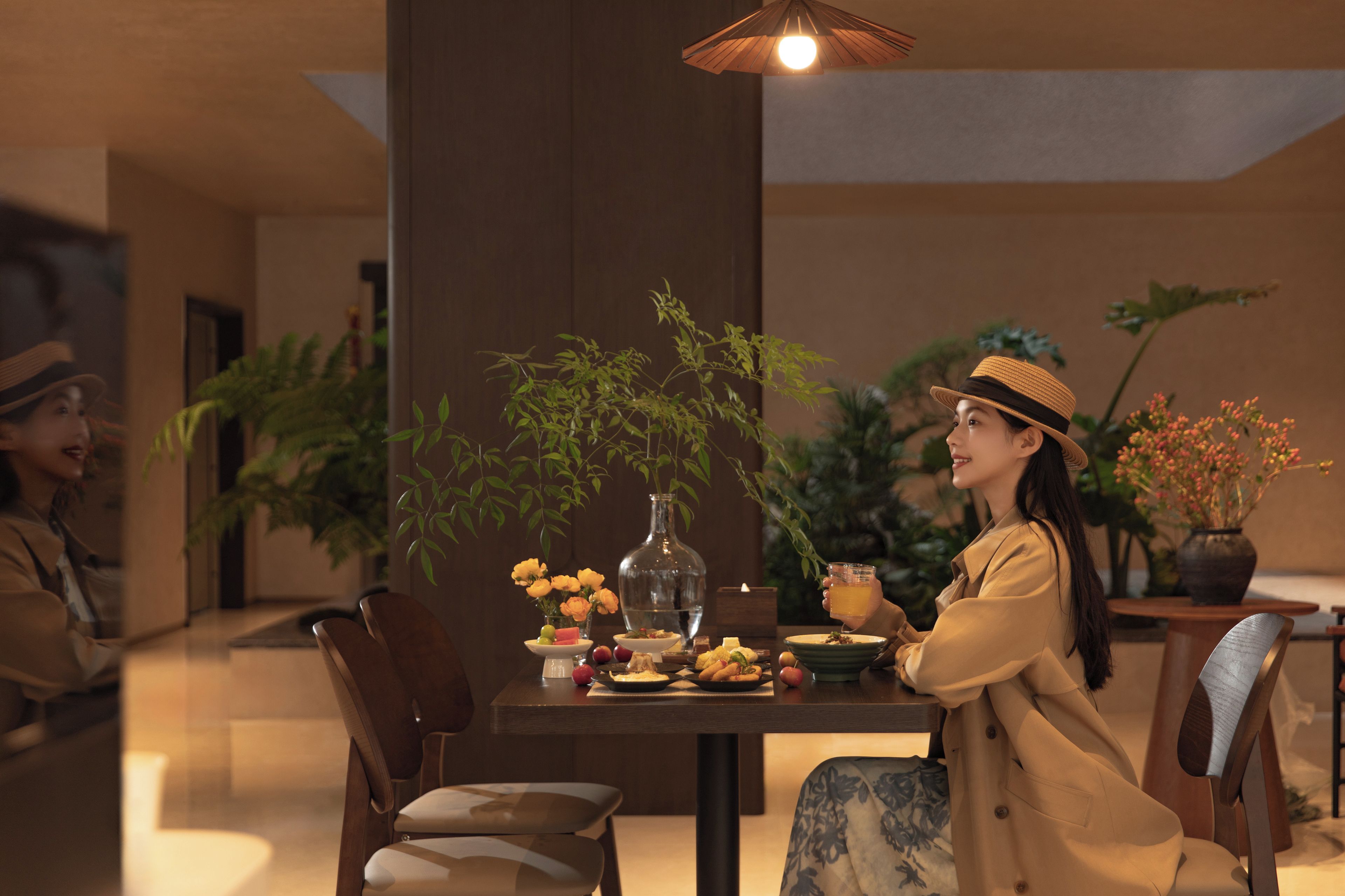 Un coin repas avec une table dressée pour deux personnes, agrémenté d’un vase avec des fleurs, d’une bouteille et de divers aliments.