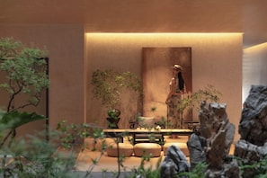 Un jardín interior tranquilo con una zona de estar, un cuadro grande en la pared y diversas plantas.