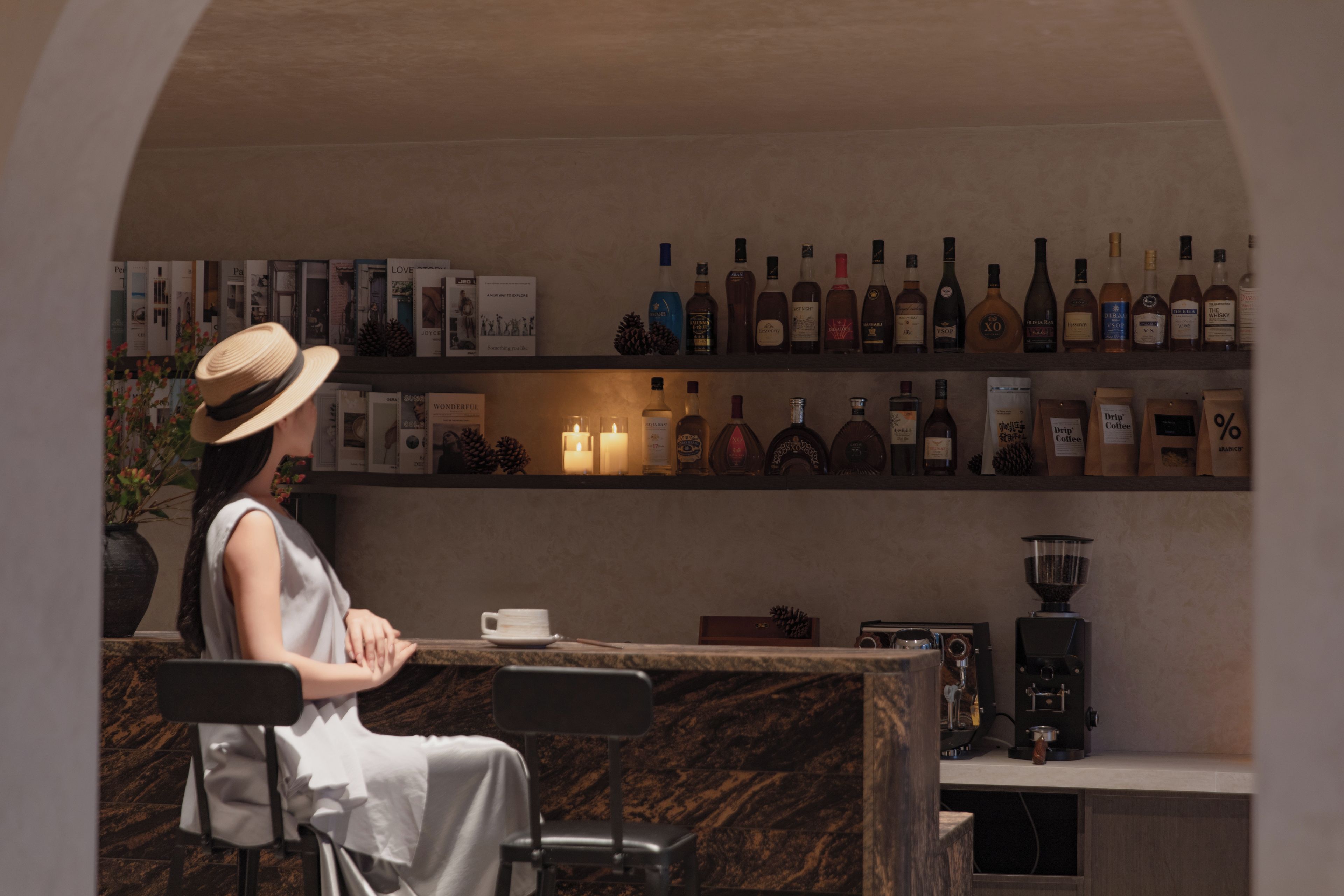 A woman seated at a bar with a drink, surrounded by shelves of liquor bottles.