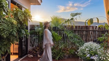 A person walking in a garden with a wooden fence, plants, and a building in the background.