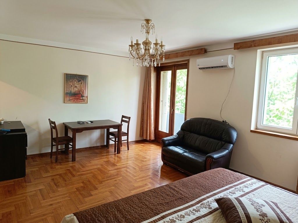 A room with a bed, a desk, a chair, a leather sofa, a chandelier, and a window with curtains.