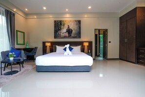 Habitación de hotel moderna con una cama grande, una zona de estar con una silla y una mesa, un cuadro en la pared y un armario.