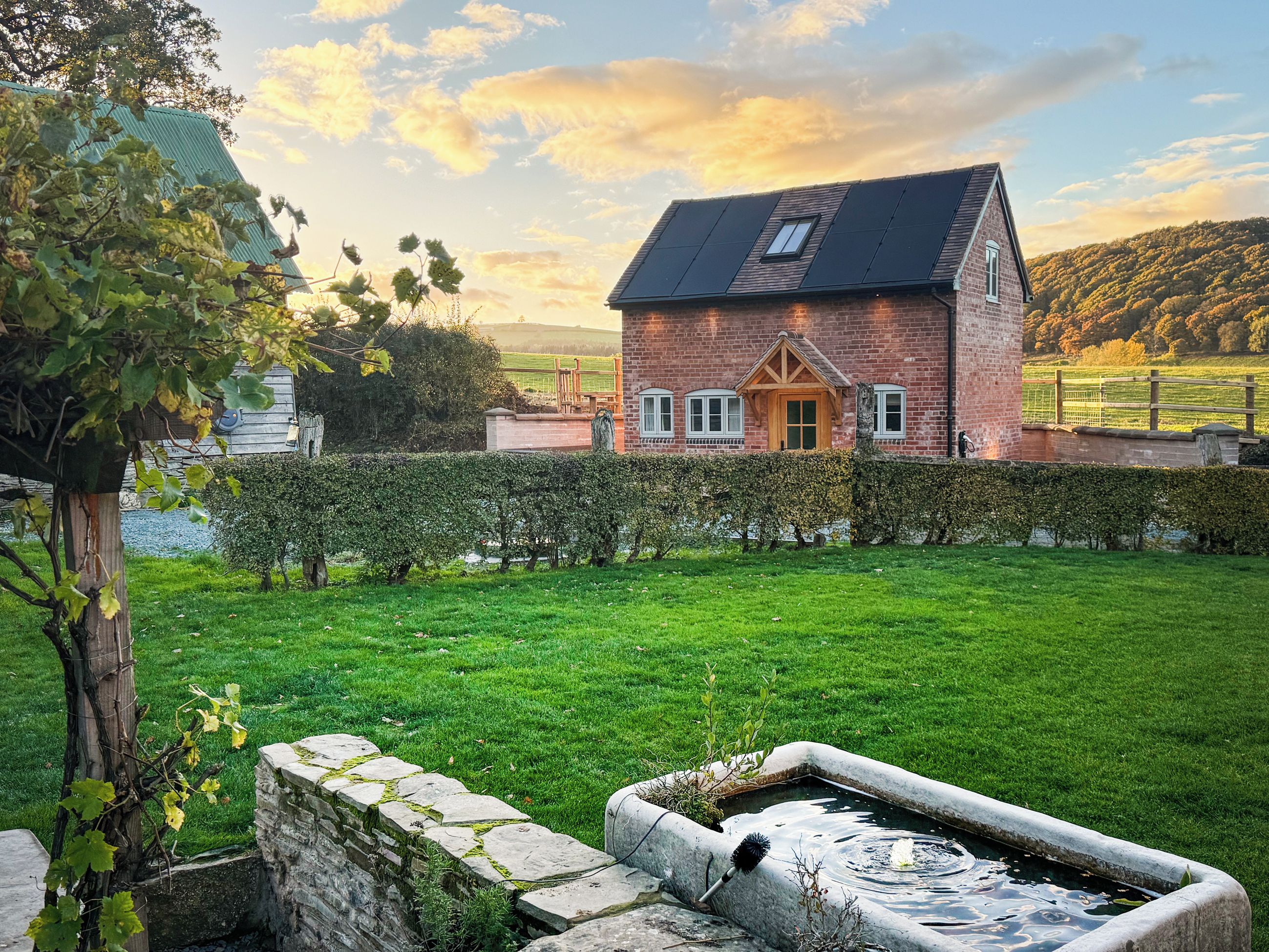 A brick house with a sloped roof, a small window, and a stone wall in the foreground.