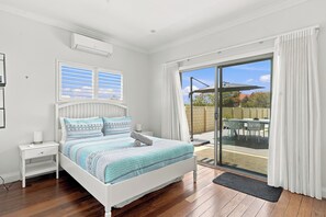 Un dormitorio con cama, mesita de noche, ventana con persianas y vistas a un patio exterior.