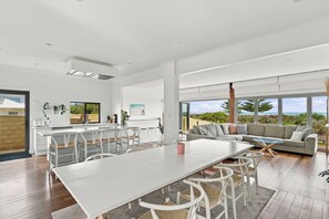 A modern kitchen with a large dining table, bar seating, and a view of the outdoors. - The Ultimate Oceanfront Entertainer (Geographe)