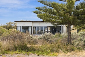 Una casa moderna con un amplio frente de vidrio, rodeada de vegetación nativa.