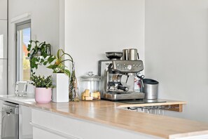 A modern kitchen with a coffee machine, a glass jar with cookies, and potted plants on the counter. - The Ultimate Oceanfront Entertainer (Geographe)
