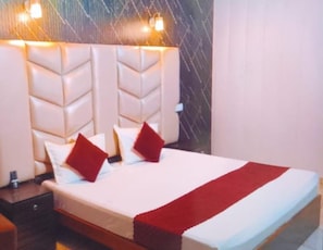 Ett hotellrum med en stor säng, två kuddar, en röd pläd och en sänggavel med inbyggda lampor.