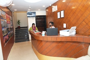 A reception desk with a curved design, a potted plant, and a poster on the wall. - Prince Malabar Residency (Secunderabad)
