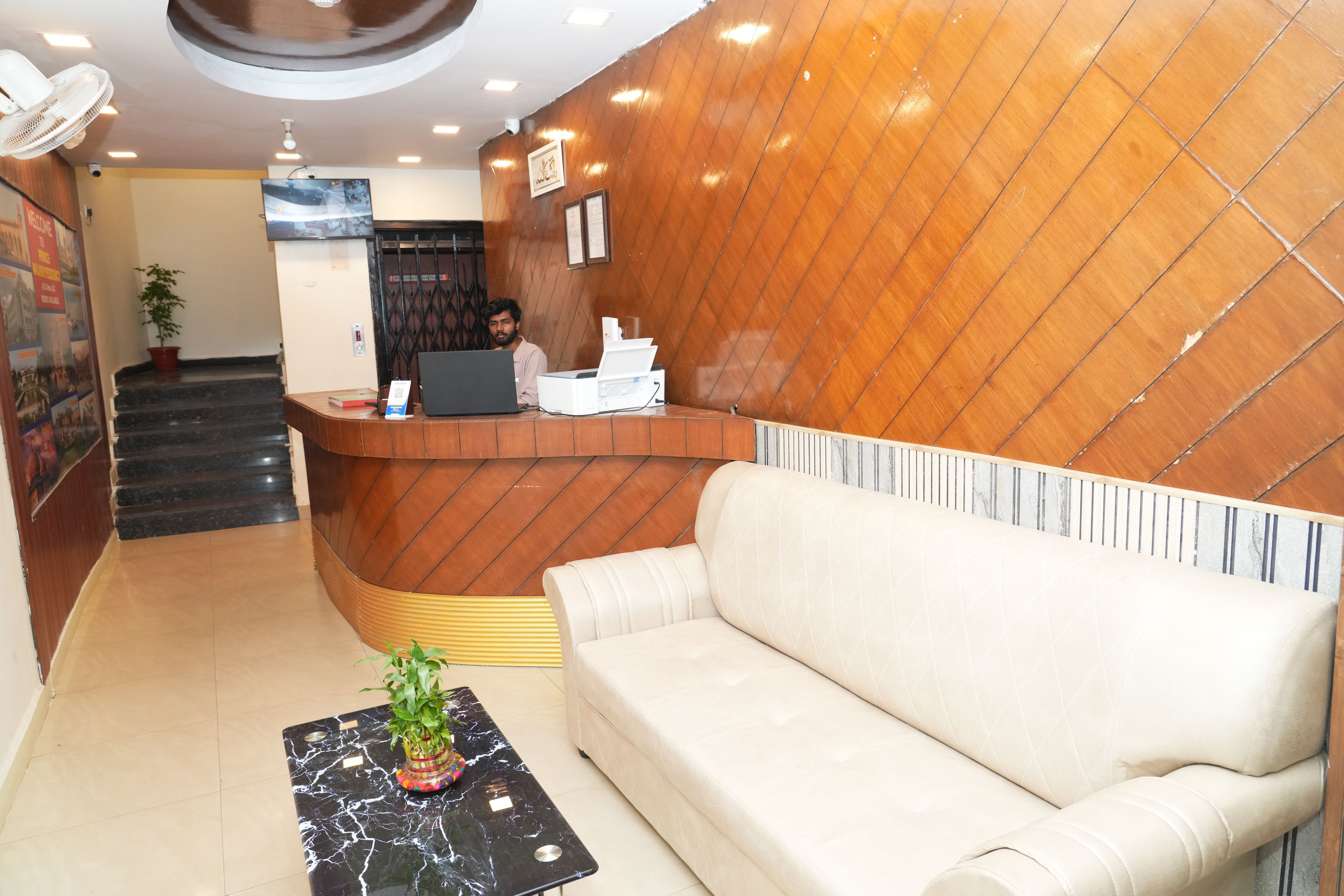 A reception area with a wooden reception desk, a laptop, a sofa, and a marble table with a plant.