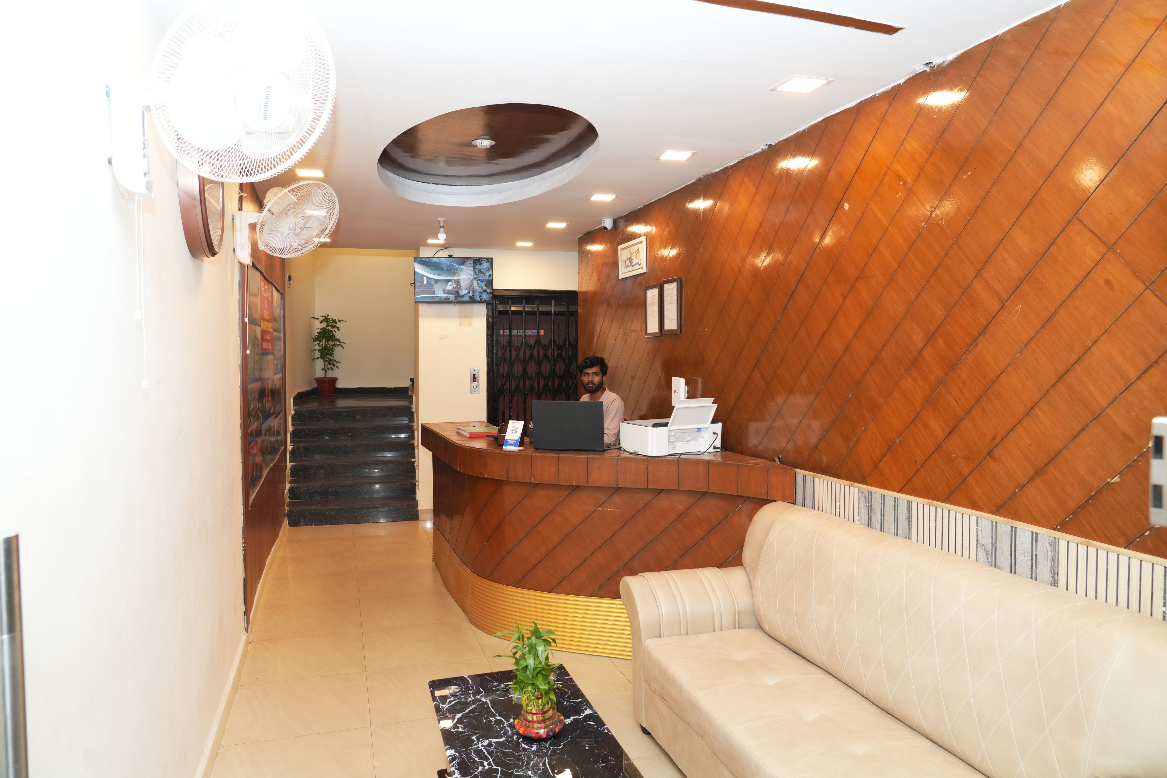 A reception area with a wooden reception desk, a sofa, a plant, and a staircase leading to an upper floor.