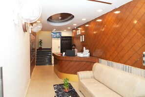 A reception area with a wooden reception desk, a sofa, a plant, and a staircase leading to an upper floor. - Prince Malabar Residency (Hyderabad)