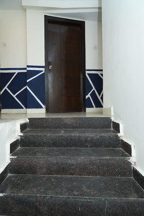 Eine Treppe führt zu einer dunklen Holztür mit einer Nummernschild, begleitet von Wänden mit geometrischen Mustern.