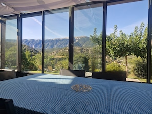 Ein Zimmer mit großem Fenster und Blick auf die Berge, einem Bett mit gemustertem Überwurf und zwei Stühlen.