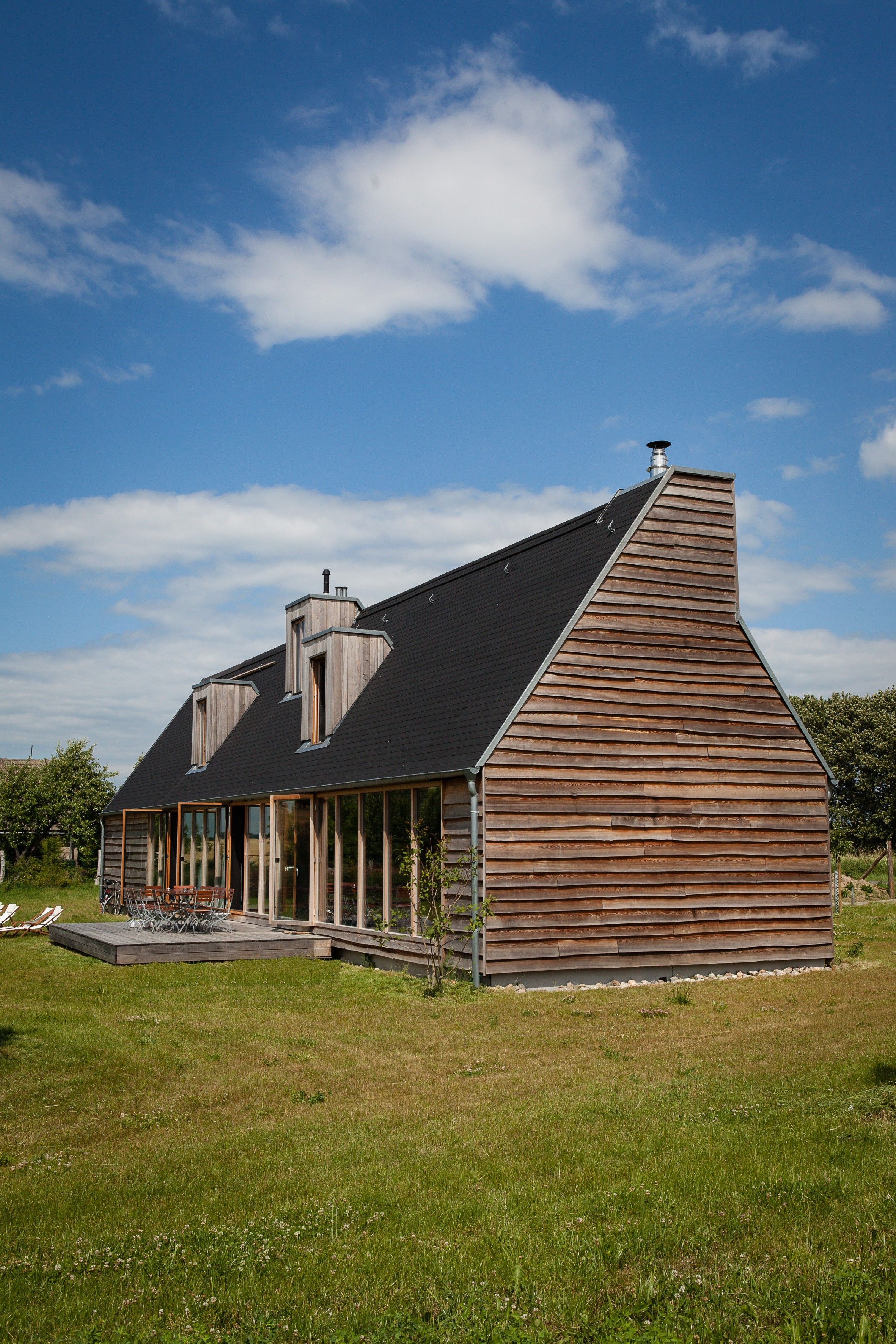 Una casa moderna con techo inclinado, fachada de madera y un porche cubierto con mobiliario exterior.