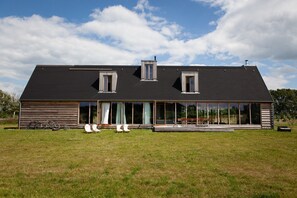 Ein modernes Haus mit großer Glasfassade, flachem Dach und einem grünen Rasen.