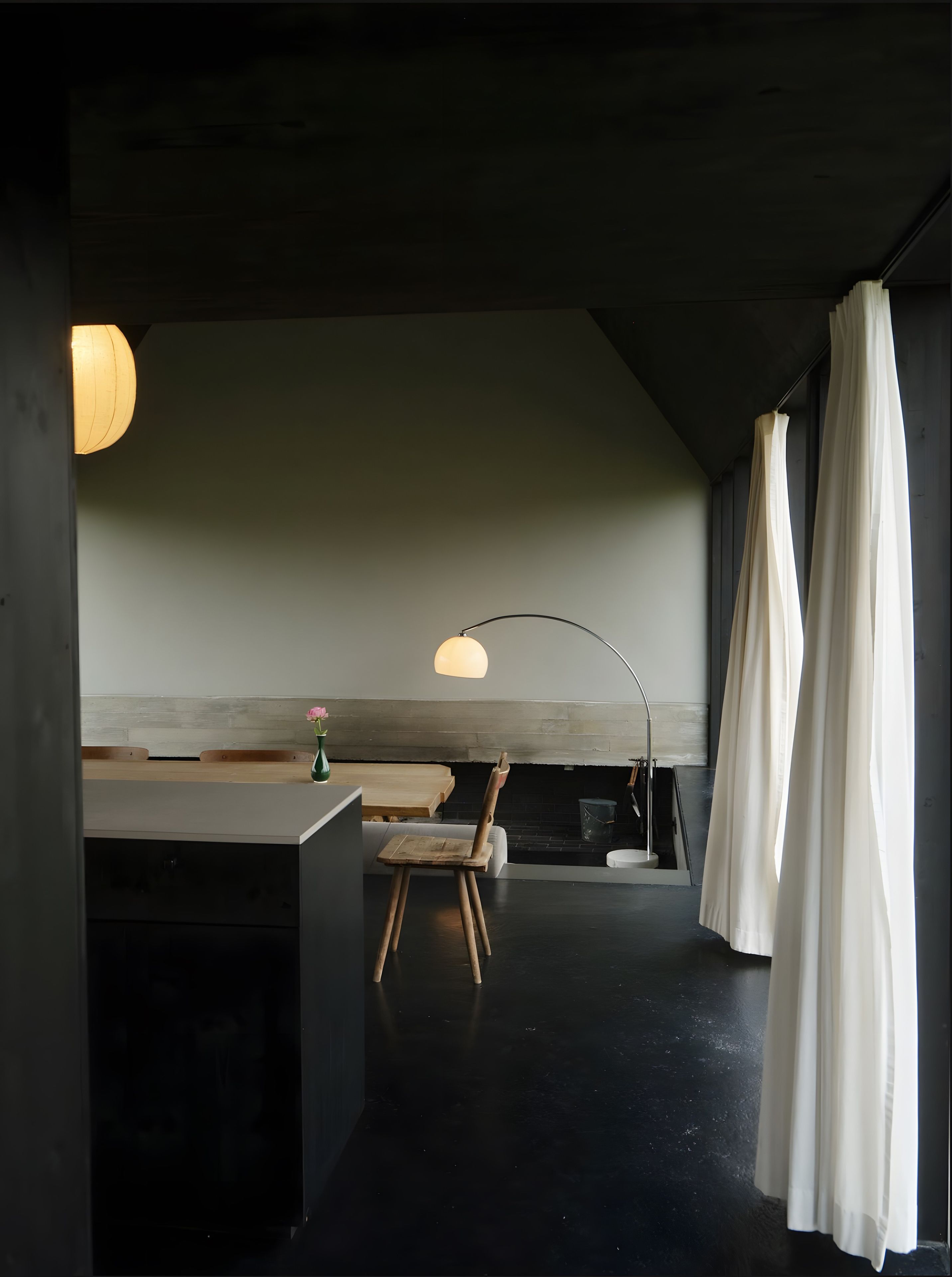 Un interior modern amb terra fosca, una cadira de fusta, una taula i una làmpada penjant.