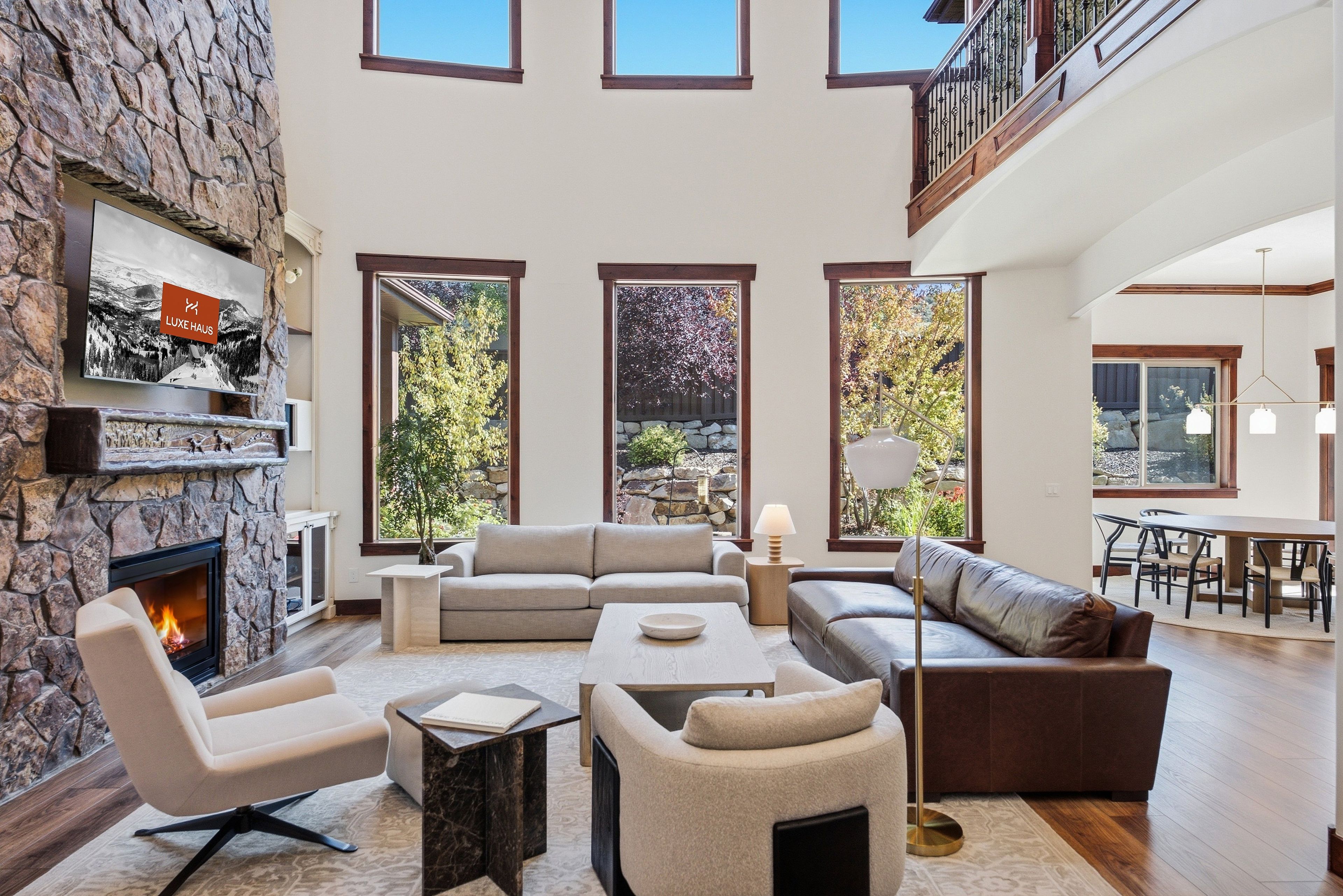 A spacious living room with a stone fireplace, multiple seating areas, and large windows offering views of the outdoors.