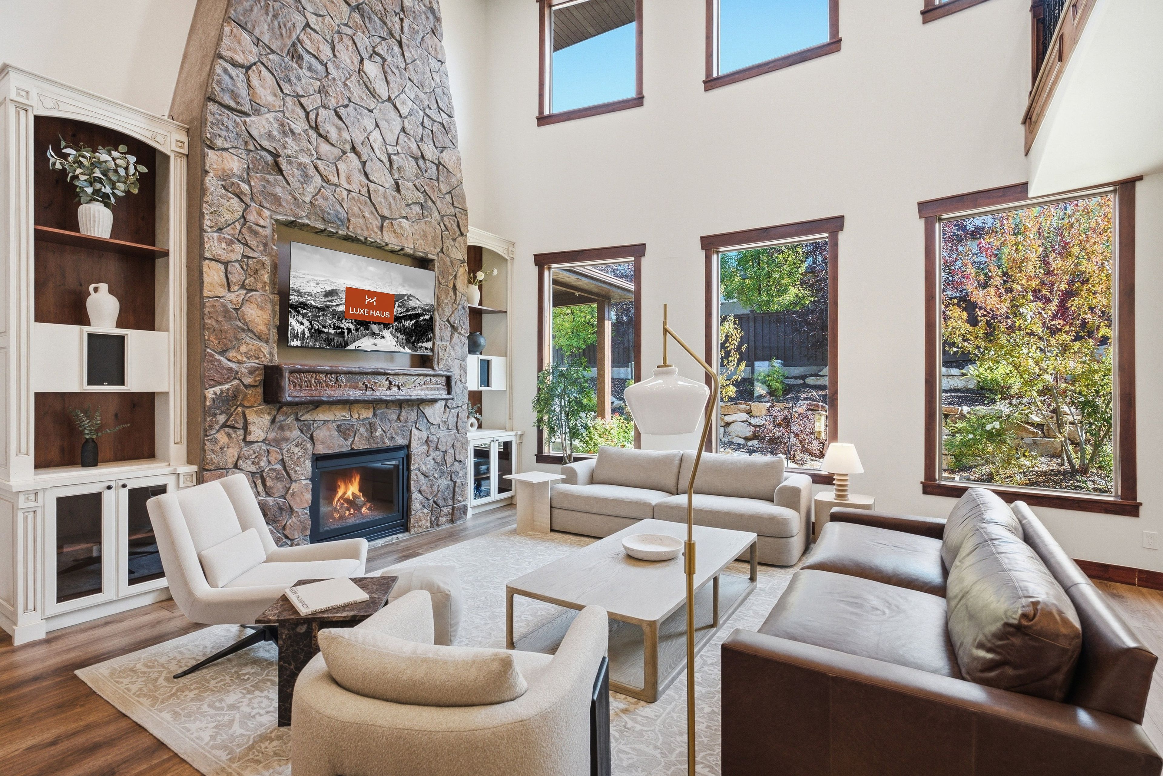 A spacious living room with a stone fireplace, comfortable seating, and large windows offering views of the outdoors.