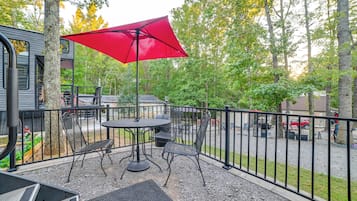 An outdoor patio with a table and chairs, a red umbrella, and a view of the surrounding trees and buildings.