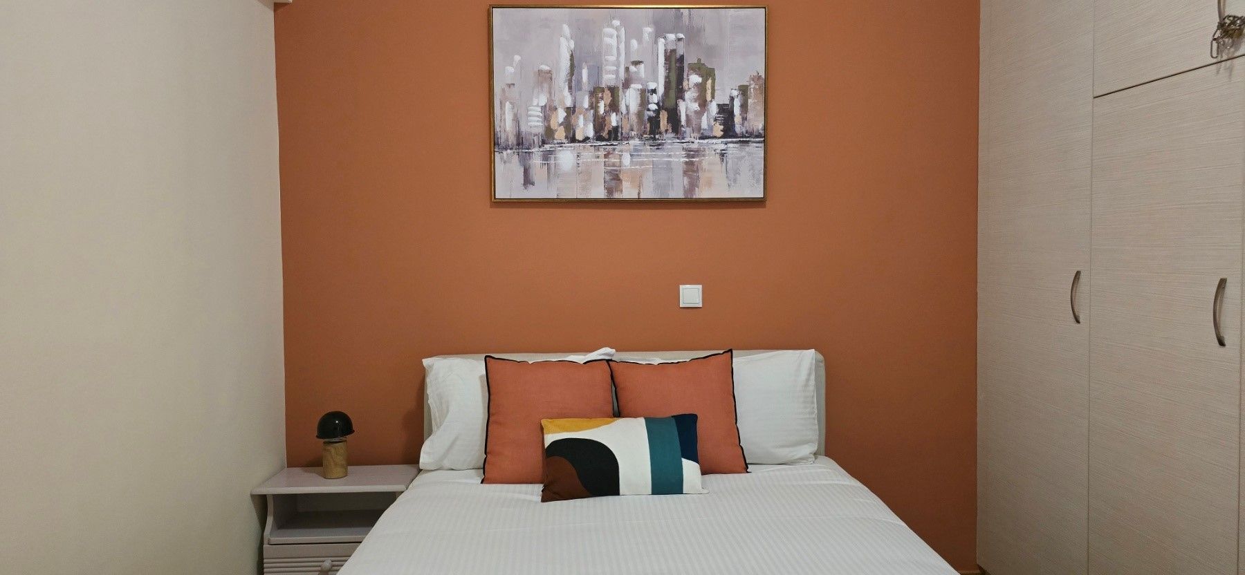A hotel room with a bed, a nightstand, a painting, and a wardrobe.
