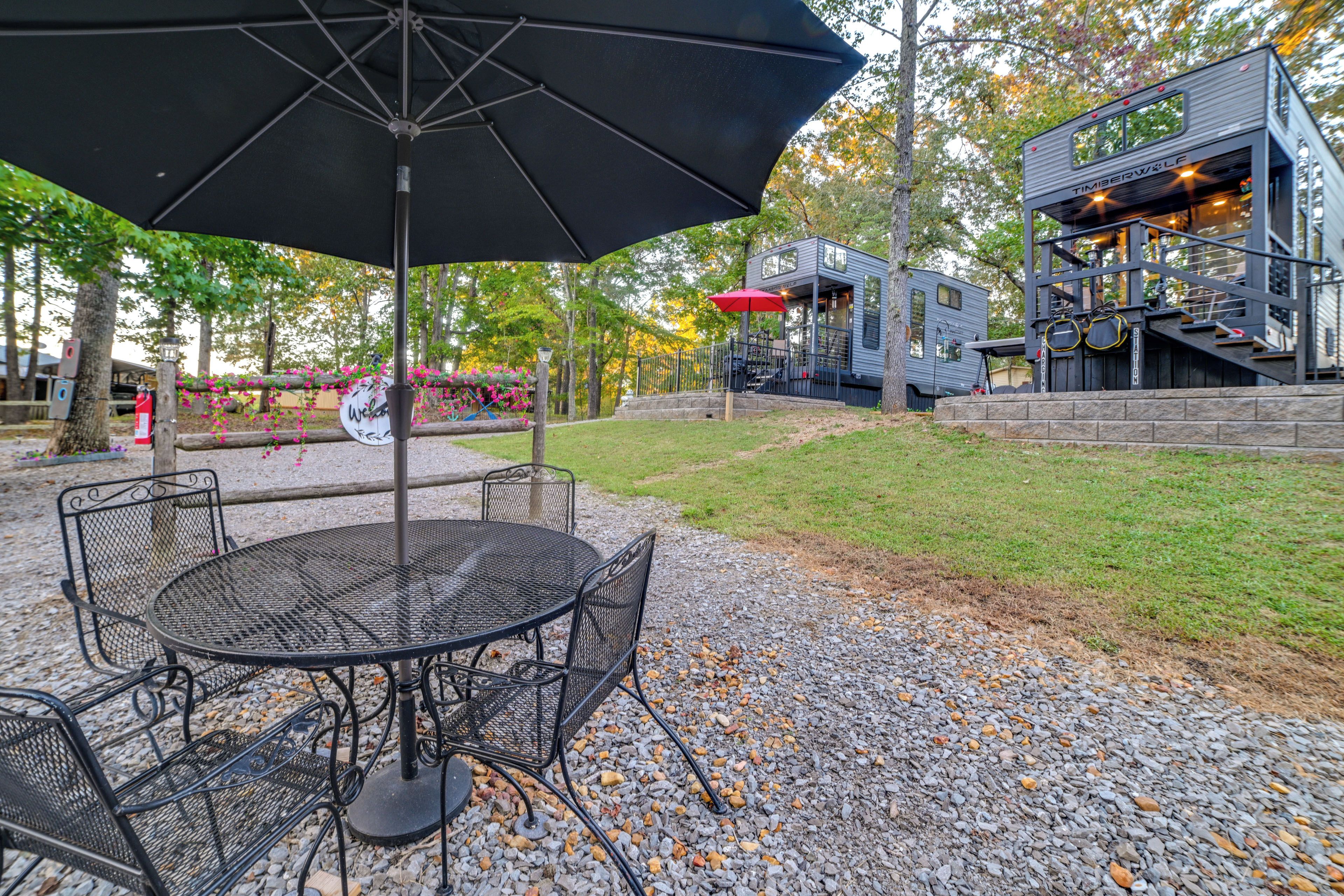 A patio area with a round metal table and chairs, an umbrella, and a small building with a staircase.