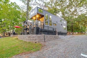 A modern, multi-level building with a stone foundation, large windows, and a covered outdoor area with a red umbrella. - Fireside Nights! Tiny Home 1 Mi to Kentucky Lake (Springville)