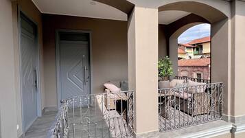 Un balcon orné de balustrades en fer forgé, une porte à motifs géométriques et une vue sur les bâtiments voisins.