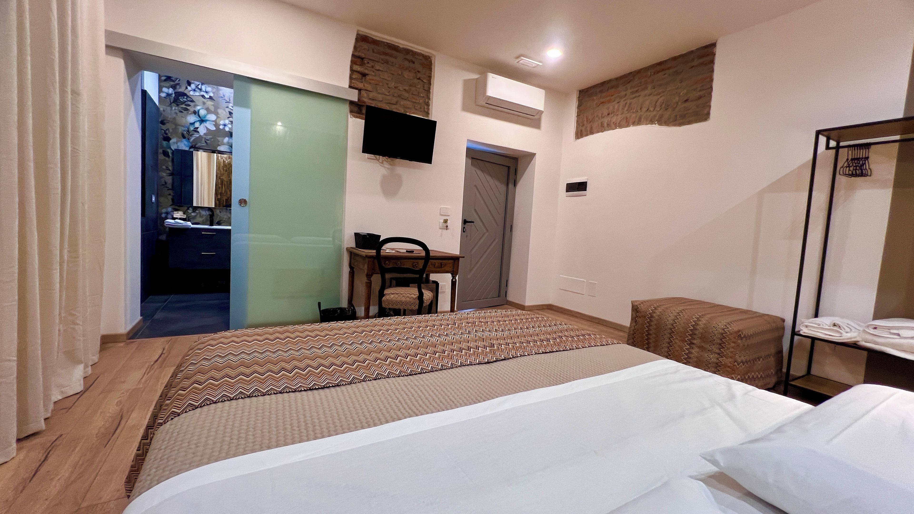 A hotel room with a bed, a desk, a chair, a television, and a wardrobe.