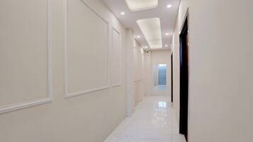 A corridor with white walls, recessed ceiling lights, and a marble floor.