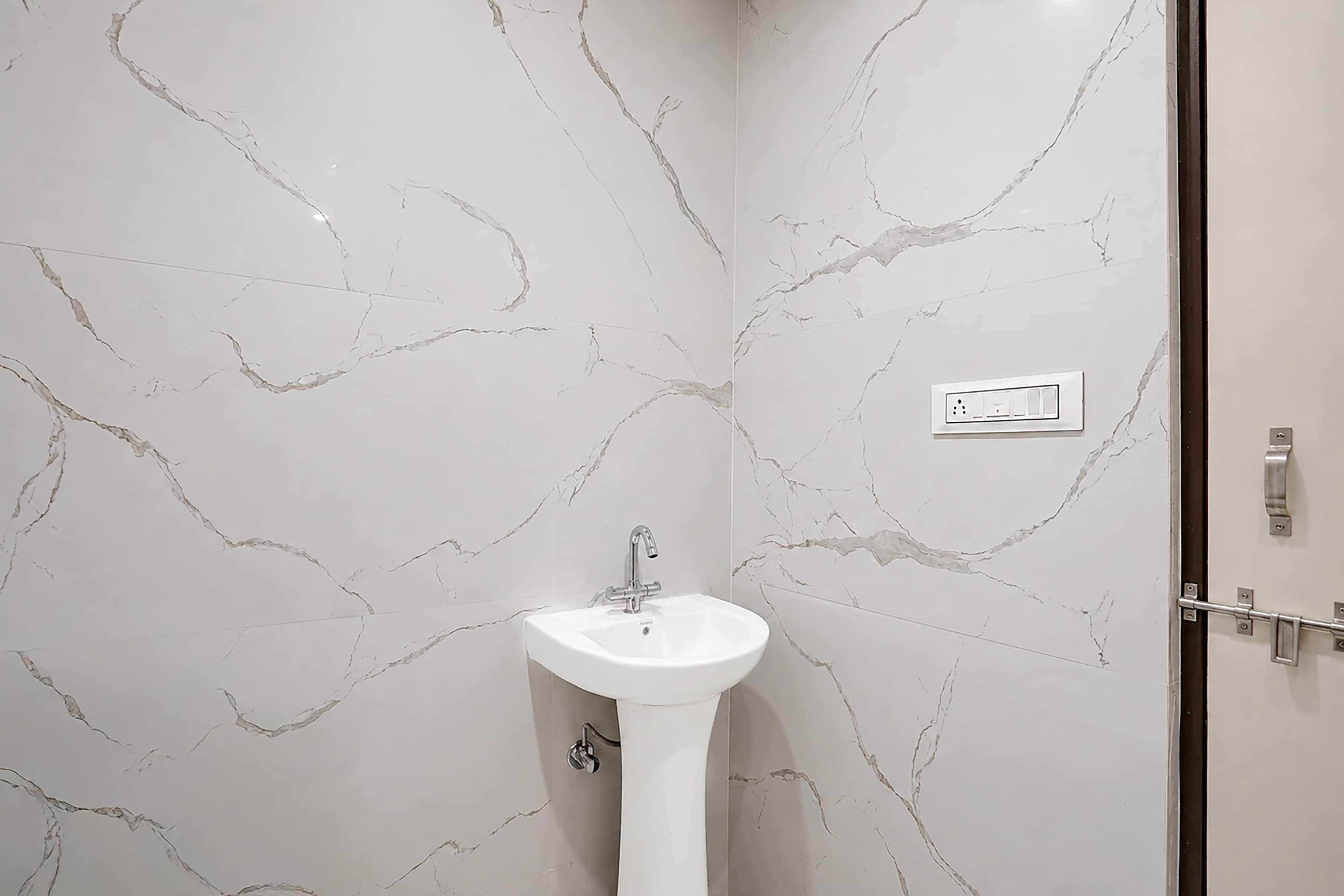 Casa de banho com parede de mármore branco e lavatório pedestal branco.