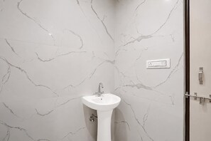 Un baño con pared de mármol blanco y lavamanos pedestal.
