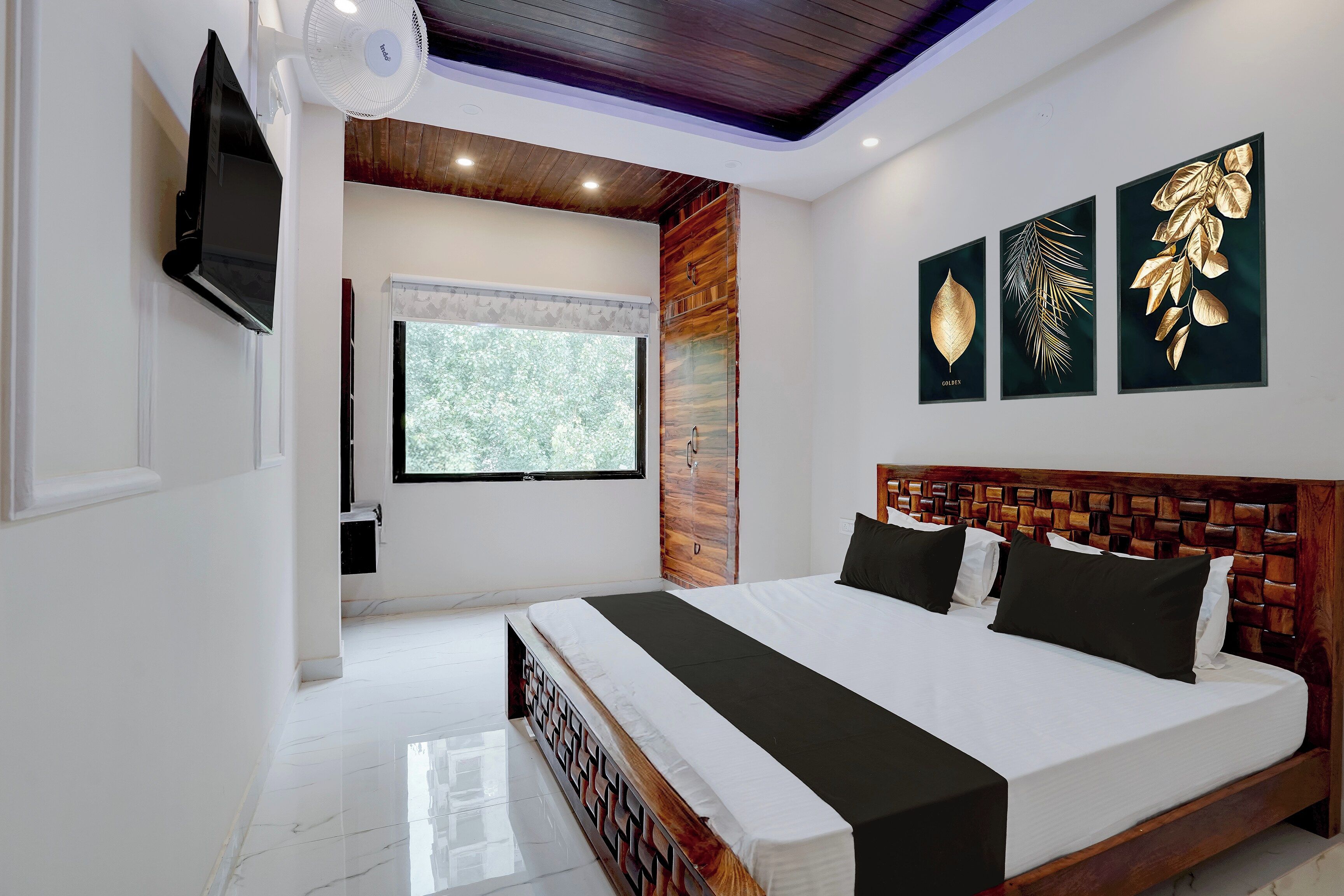 Quarto moderno com uma cama grande, uma TV fixada na parede e três obras de arte com folhas emolduradas.