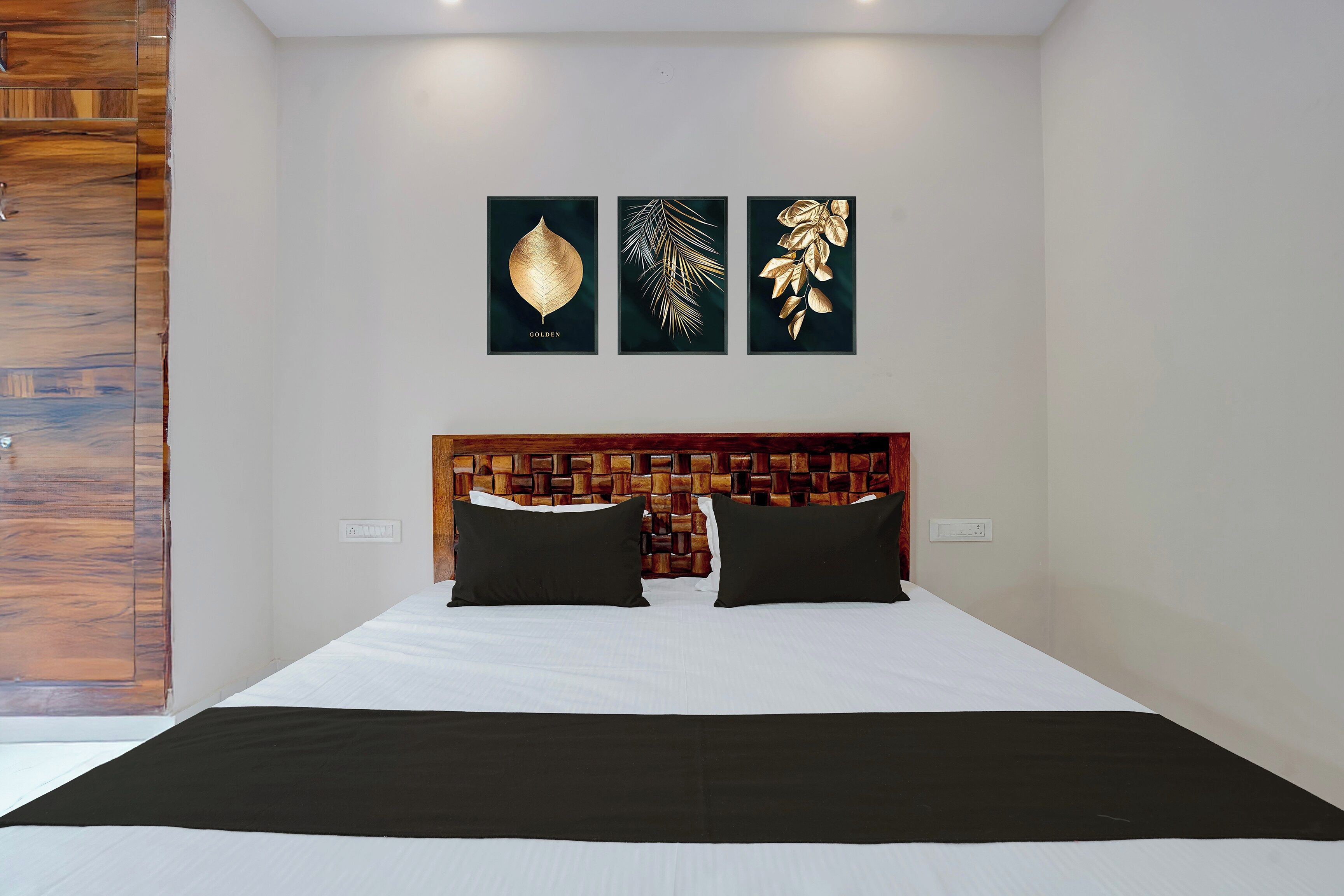 A bedroom with a wooden headboard, a bed with white bedding, and three framed artworks on the wall.