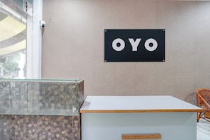 Ein Empfangsschalter mit Glastischplatte, einer weißen Theke und einem Schild mit der Aufschrift 'OYO' an der Wand.