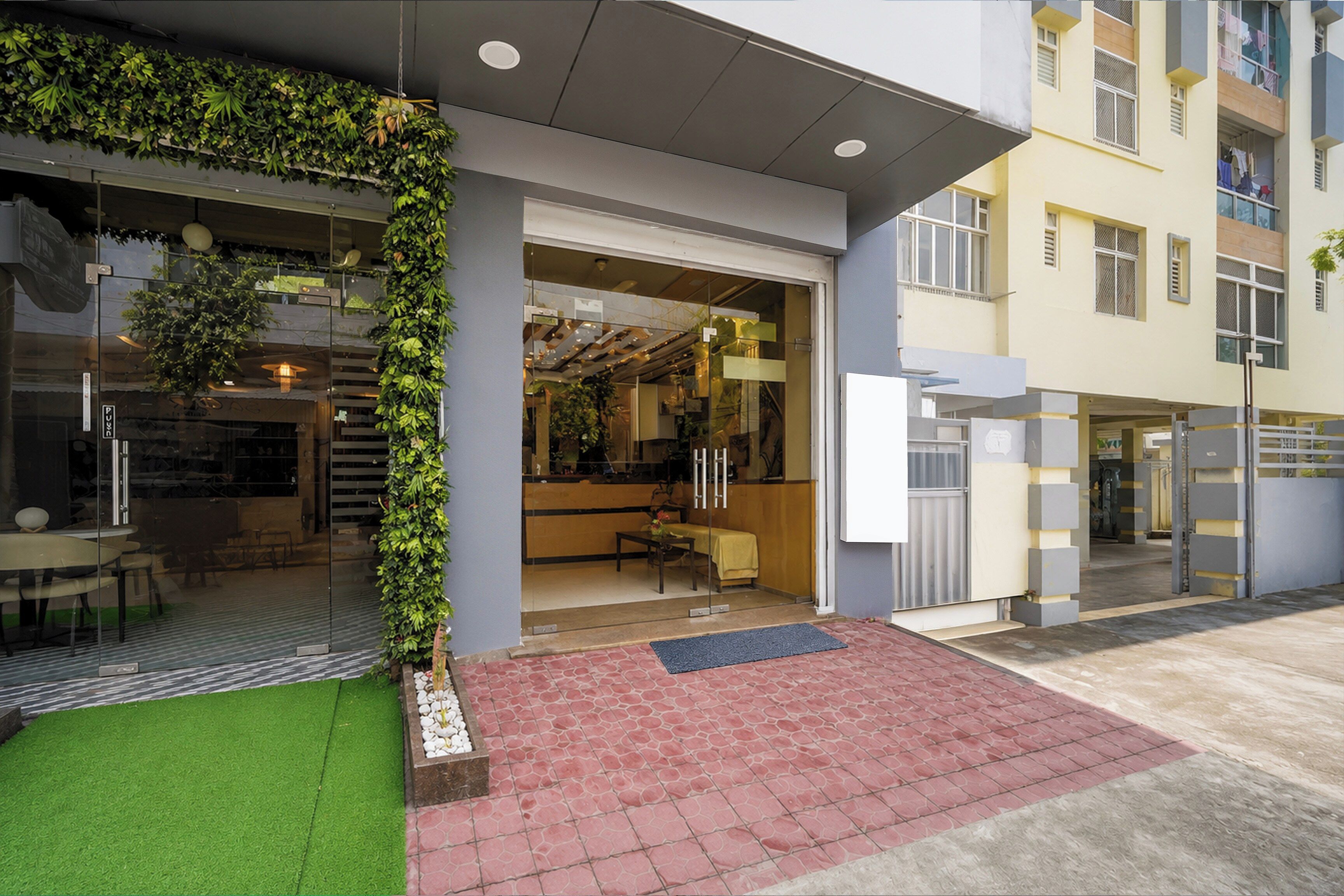 A modern building with a glass facade, a green wall with plants, and a brick-paved entrance.