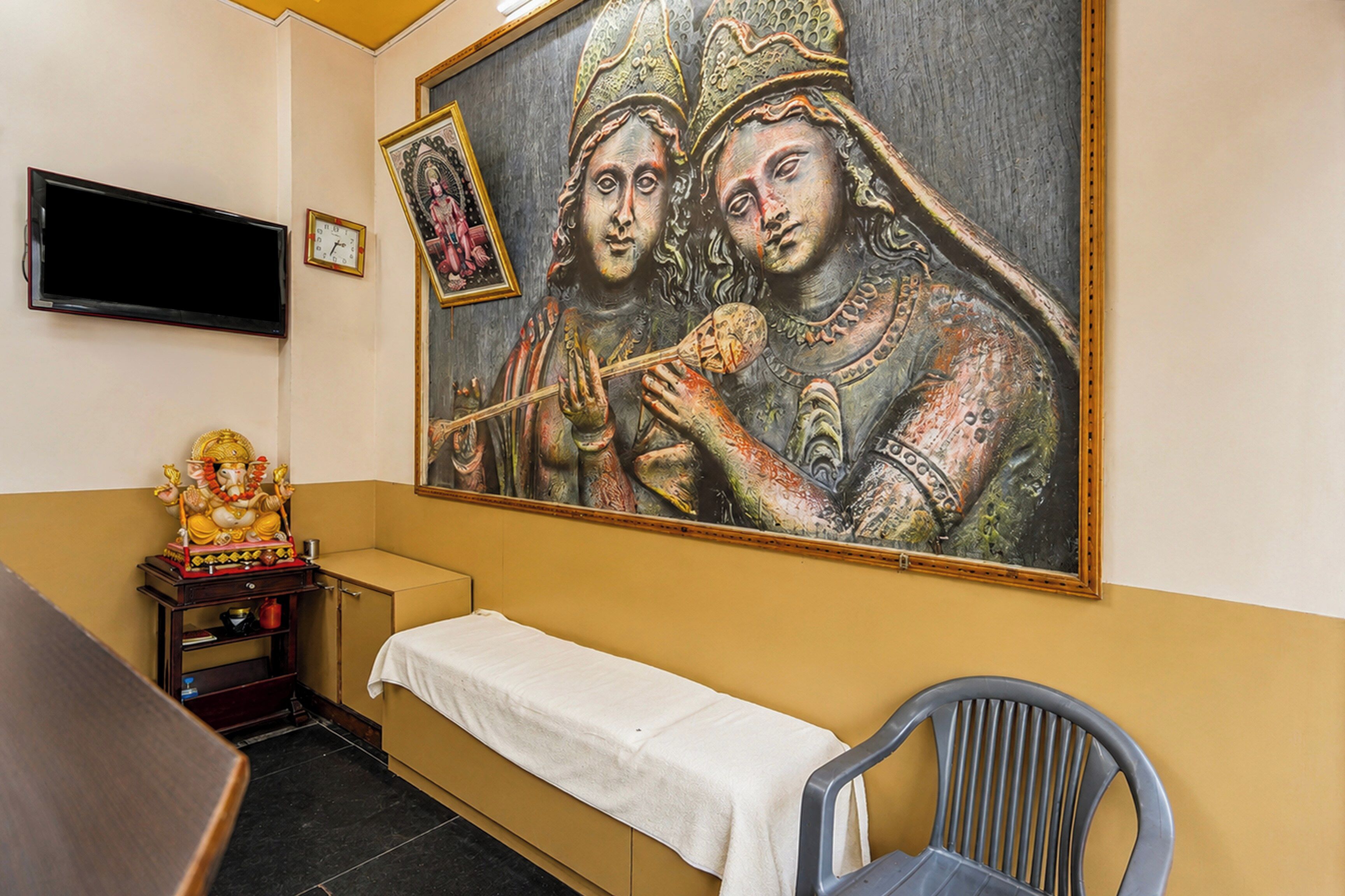 A room with a bed, a chair, a television, and a wall with a painting.